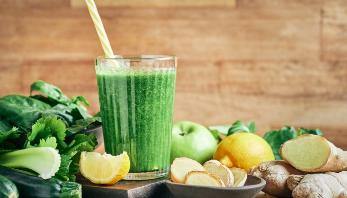 Smoothie frais et sain aux légumes verts et au gingembre, servi dans un verre avec du citron pour des cheveux resplendissants.